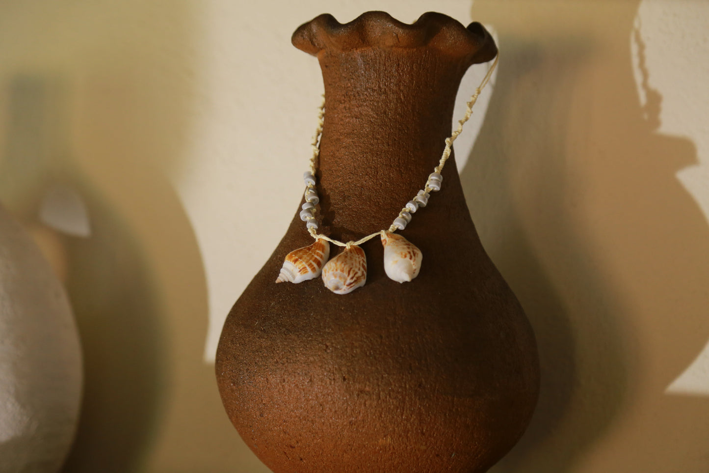 Trois Tessellées Vân Cam necklace draped on terracotta vase